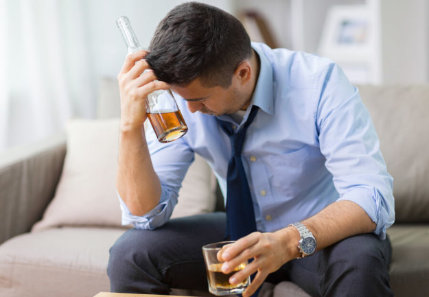 The Effects of Drinking on Others A male alcoholic drinking at home with a glass and bottle of whiskey.