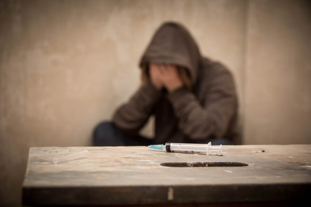 What Does a Heroin User Look Like? A heroin syringe on a table with a man struggling with addiction in the background.
