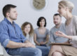 A man struggling with substance abuse talking to an addiction professional with his family in the background.
