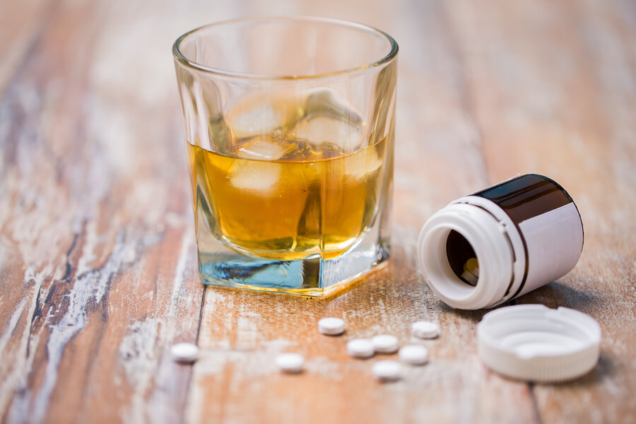 The Dangers of Taking Opioids While Drinking A glass of alcohol and an open bottle of opioids sitting on a table.