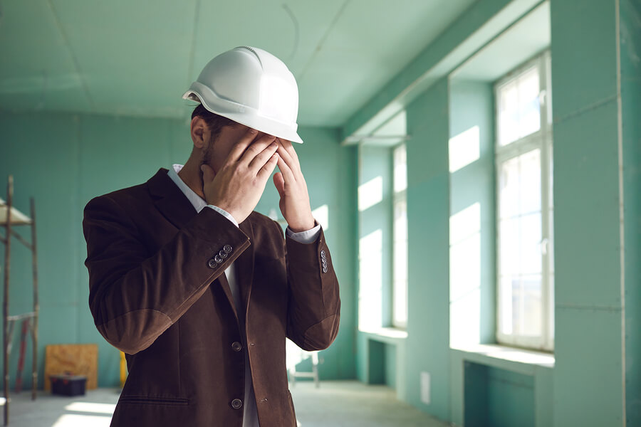 A stressed-out construction foreman covering his face with his hands.