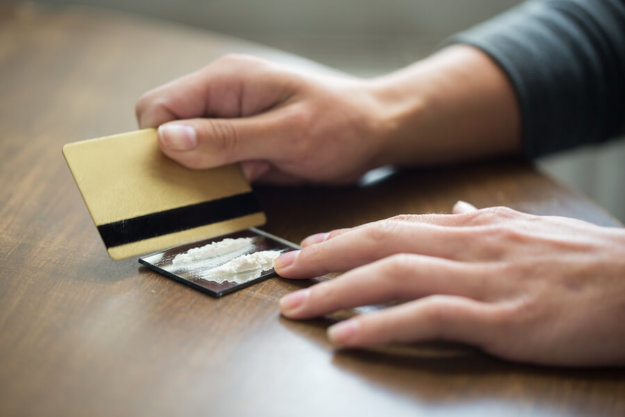 What Does Cocaine Do to The Body A man using his credit card to cut lines of cocaine on his kitchen table.