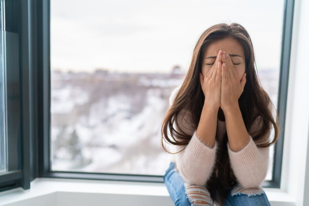 A woman sitting in her apartment with her hands holding her head struggling with depression.