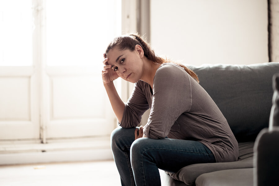 A woman in recovery sitting on a couch looking anxious and distressed.