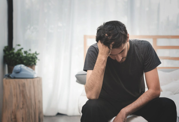 A man suffering from an anxiety disorder holding his head in bed.