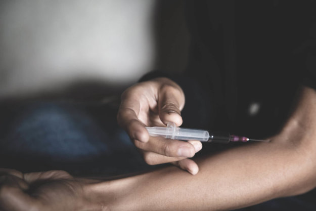 A man injecting heroin into his arm with a syringe.